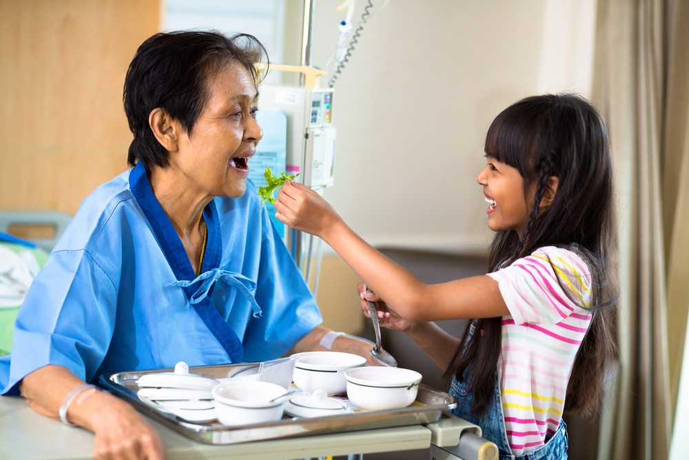 Granddaughter is feeding her grandmother with vegetable in the hospital
