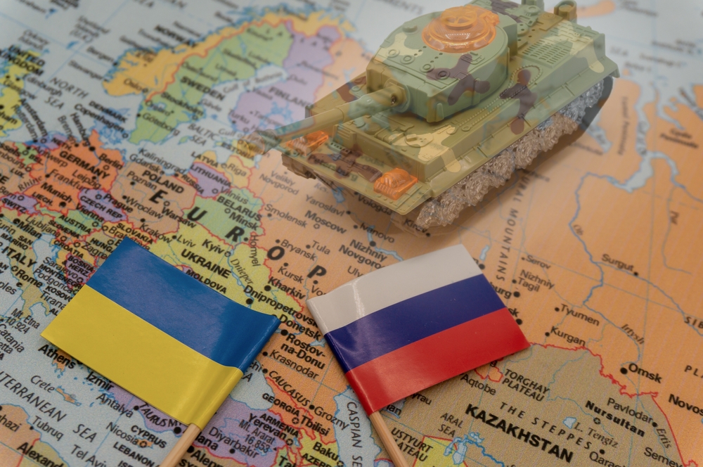 Ukrainian and Russian flags placed on a map of Europe. Ukraine crisis and Conflict. Double exposure image of blurred tank.Choose to focus on the flags. International situation theme