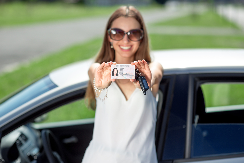 Young woman showing a key and license in front of the car. Girl pass successfully driving exam.
