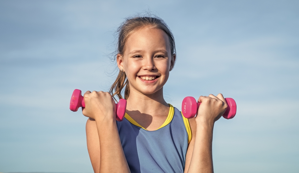 workout outdoor. teen girl use dumbbell. sporty kid in sportswear do lifting exercise.