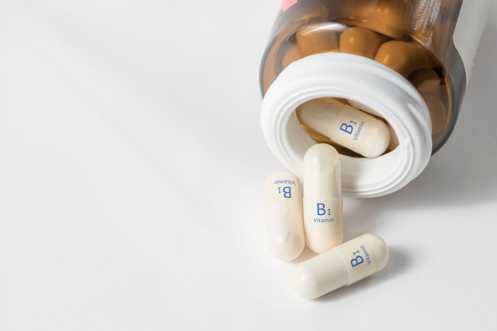 Vitamin B1. Thiamine vitamins in capsules for the work of the heart and healthy nerve cells. White capsules with vitamin B1 or thiamine are scattered on the table from a bottle with copy space.