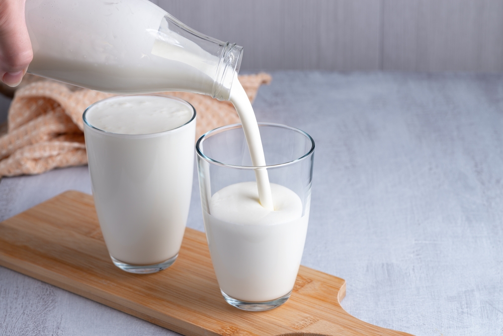 Pouring homemade kefir, buttermilk or yogurt with probiotics. Yogurt flowing from glass bottle on light background. Probiotic cold fermented dairy drink. Trendy food and drink. Copy space.