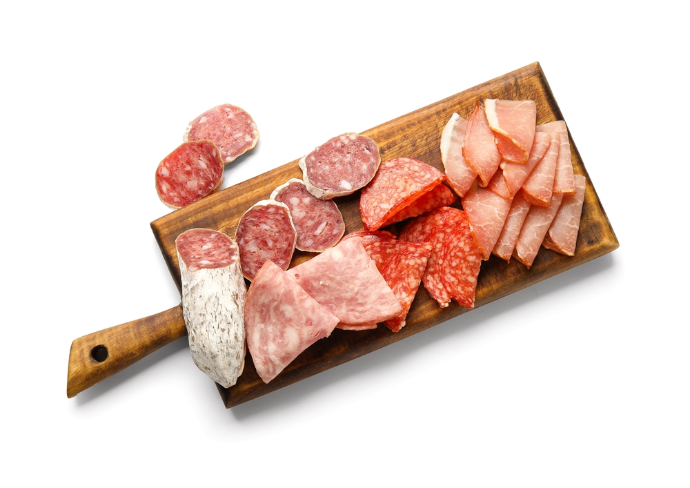 Wooden board with assortment of tasty deli meats isolated on white background
