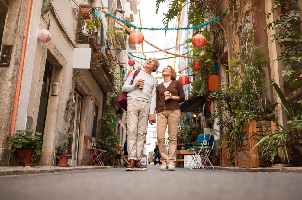 Full Length Shot Of Happy Senior Tourists Couple Walking Holding Paper Coffee Cups Sightseeing Outdoors, Enjoying Vacation In Europe. Spouses Traveling On Retirement. Tour Offer Advertisement