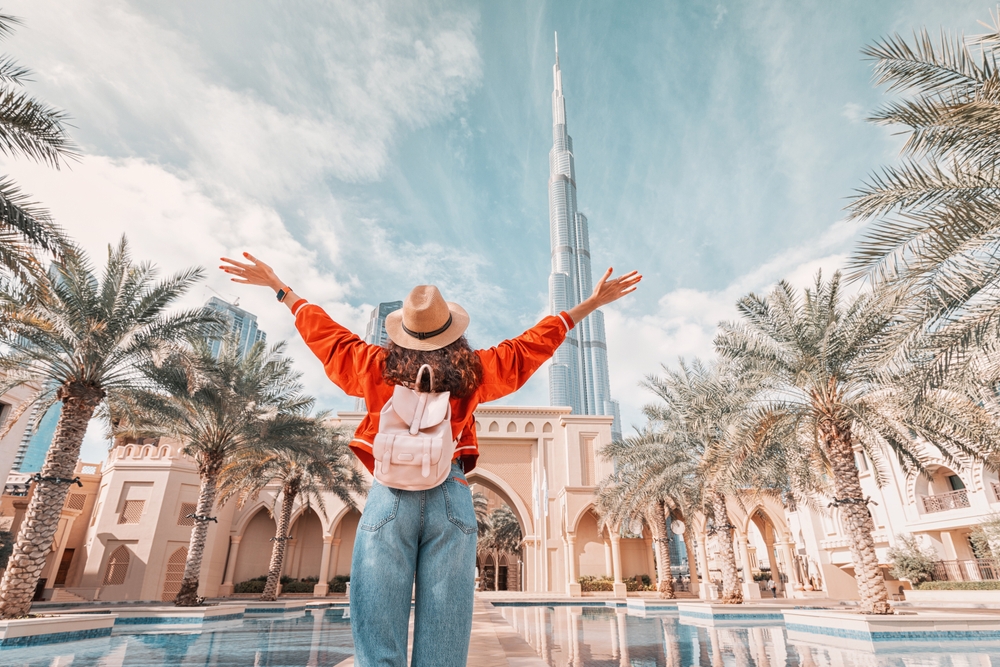 From behind, you can see the traveler girl arms spread wide as she take in the incredible view of the Burj Khalifa and the Dubai skyline.