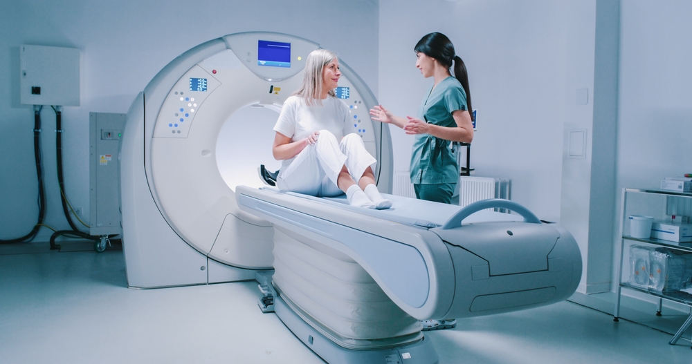 Doctor and patient are discussing results of tomography eximination. Female doctor is scrolling scrren of tablet and analizing scans of brain. Woman is sitting and listens attentively to doctor.