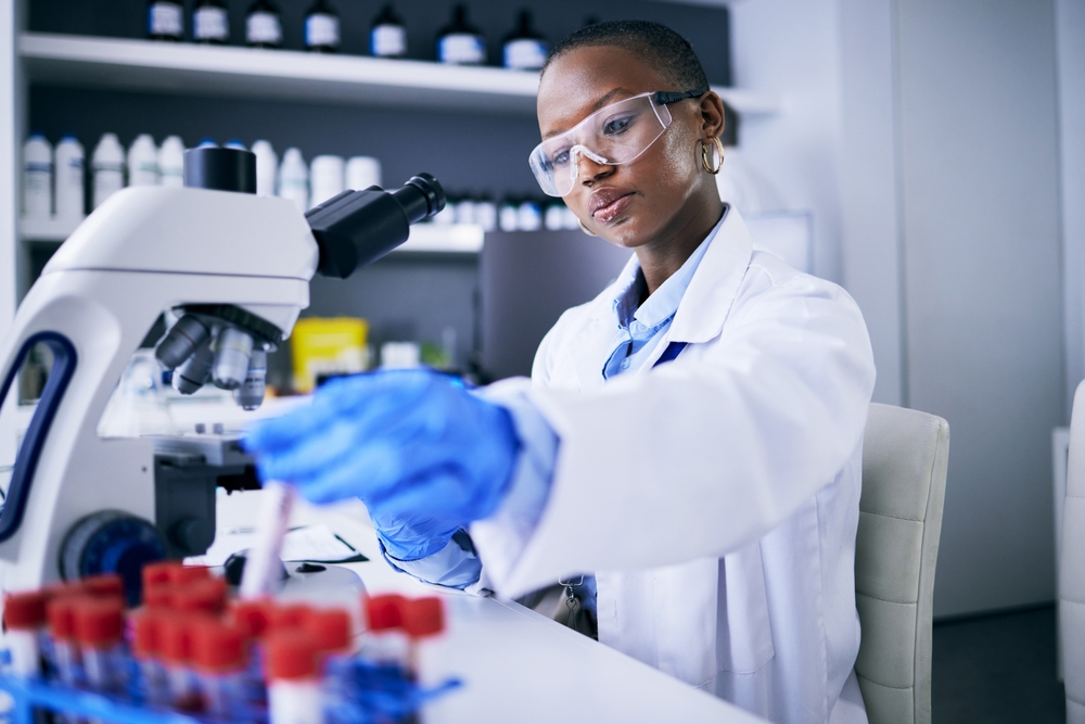 Blood test, microscope and science woman in laboratory for cancer research, medical analysis and dna test. Biotechnology, red liquid and scientist, doctor or african person, check tube in healthcare
