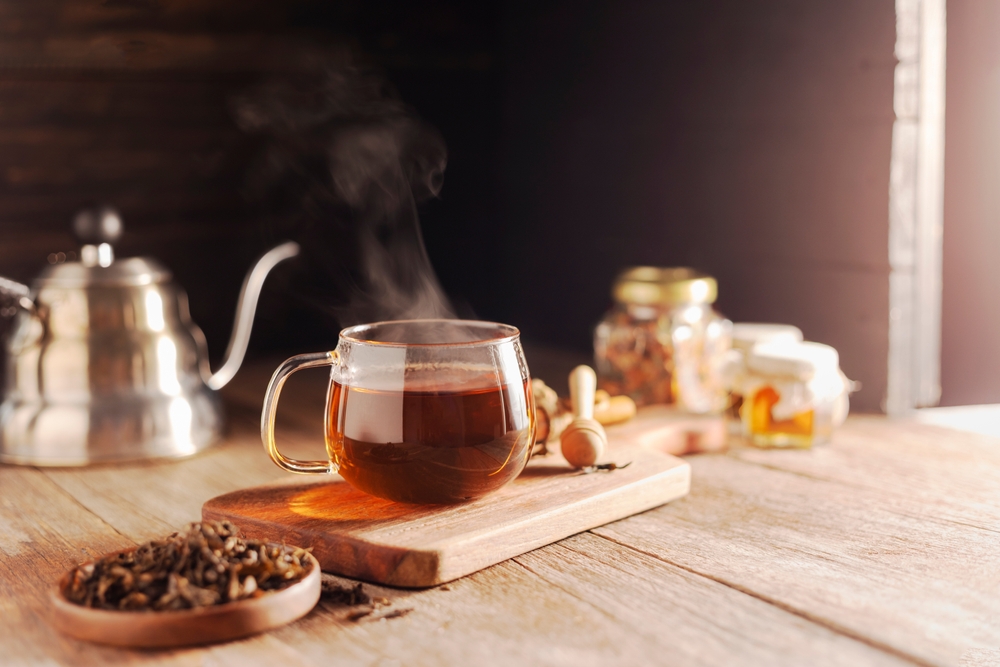 Cup or tea glass Hot brew and dried tea leaves on a wooden plate, placed on a wooden table, on a dark black background.