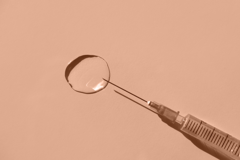 Medical syringe and transparent liquid on a beige background. Flat lay, place for text. Peach fuzz is color of year 2024.