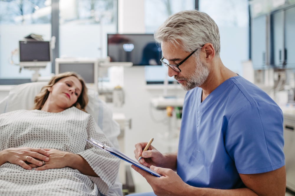 Doctor talking with worried patient before surgery, writing medical document. Emotional support before surgery. Friendly male doctor reassuring patient.