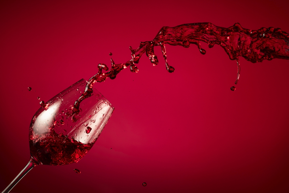 Glass and red wine splash on a red background. Copy space.