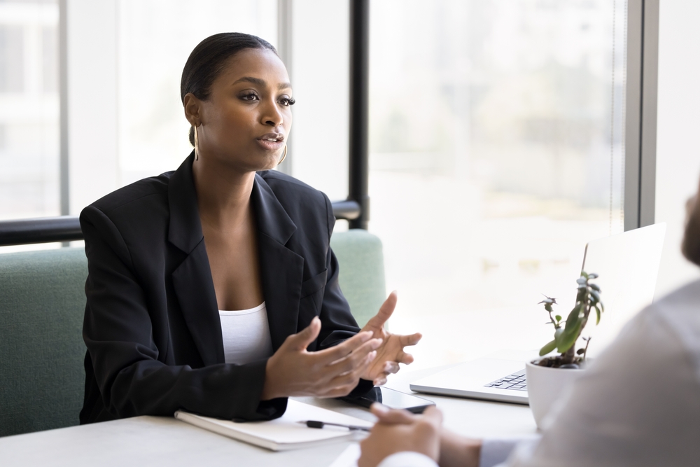 Serious beautiful African American consultant woman talking to customers at business meeting, sitting at cafe table, speaking. Real estate agent, bank broker, financial advisor giving consultation