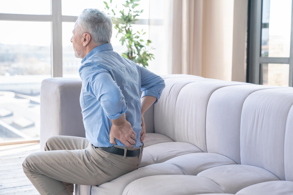 Senior caucasian old elderly man suffering from back pain at home. Rheumatism, ache, health problems. Sedentary lifestyle. People, healthcare and problem concept