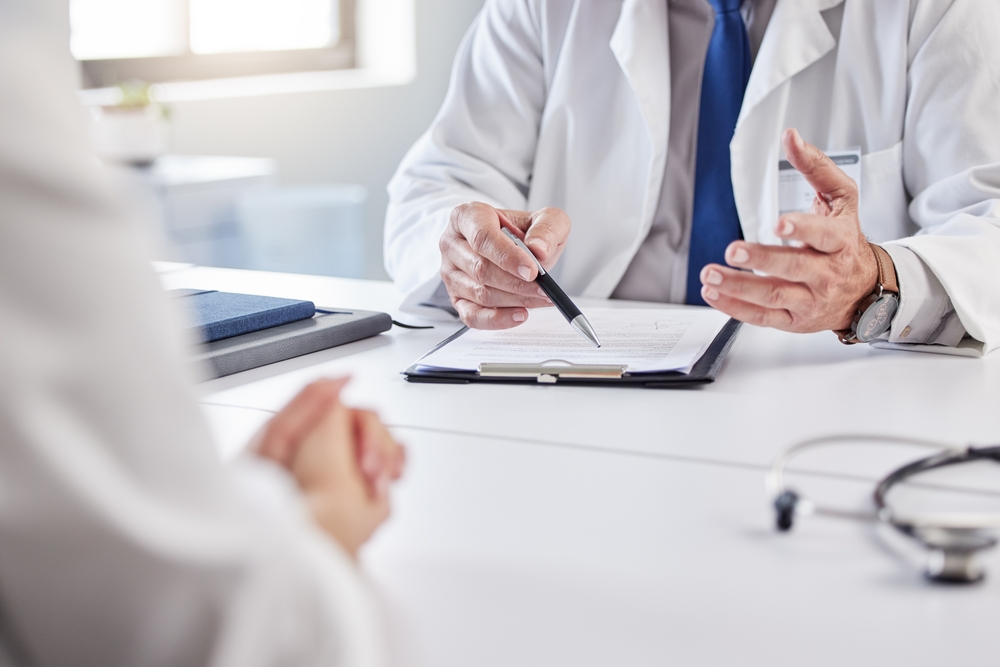 Hands, doctor and patient with consultation in clipboard for medical history, information or report. People, medic and documents for admin, insurance and checklist for healthcare service in hospital