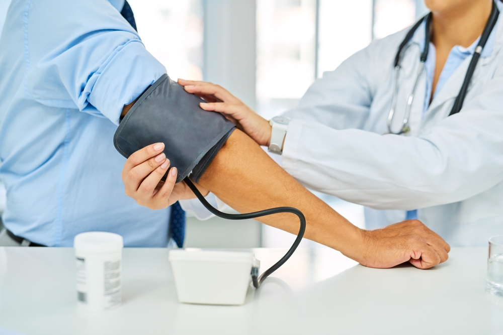 Blood pressure, hospital and hands of doctor with patient in office for medical consultation. Hypertension, healthcare and nurse with heart rate machine on man for cardiology checkup in clinic.