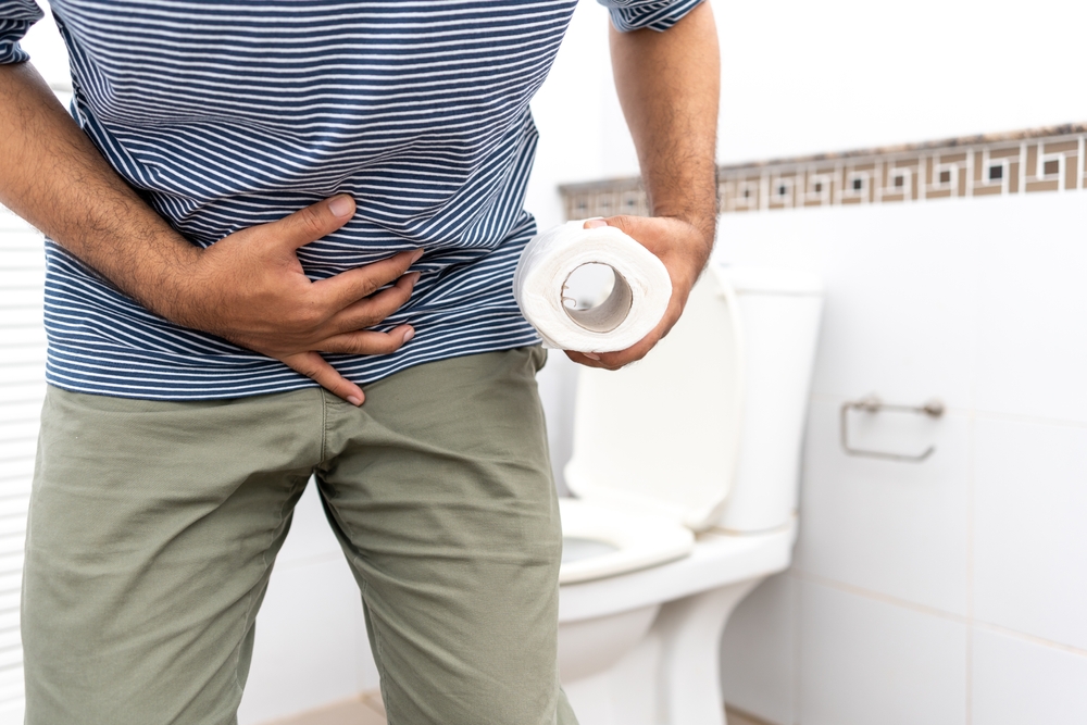 Male suffers from diarrhea holds toilet paper roll in front toilet bowl. Man squeezing tissue with diarrhea excreting in toilet. Hand holding a roll toilet paper is feeling pain with constipation.