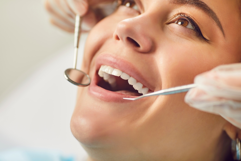 Close-up cropped shot of young woman at the dentist's chair during a dental procedure looking up and smiling. Dentist examining patient's teeth in modern clinic. Healthy teeth and medicine concept.