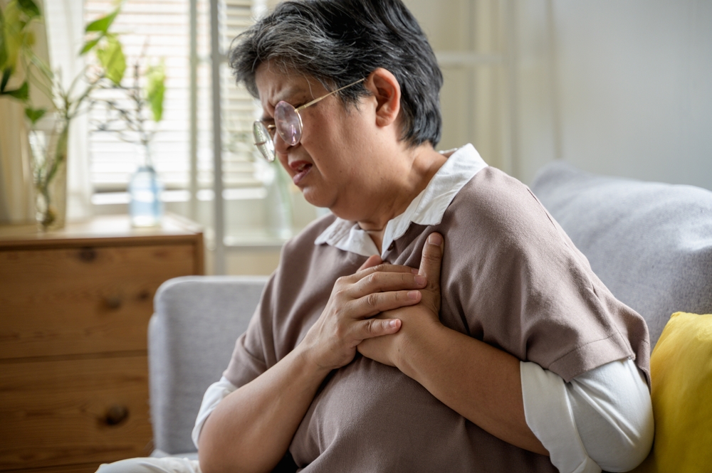 Senior elder woman has a heart attack symptom alone in her house living room. Senior elder Asian woman has a severe heart attack symptom breast pain in her house. Senior health or health care concept
