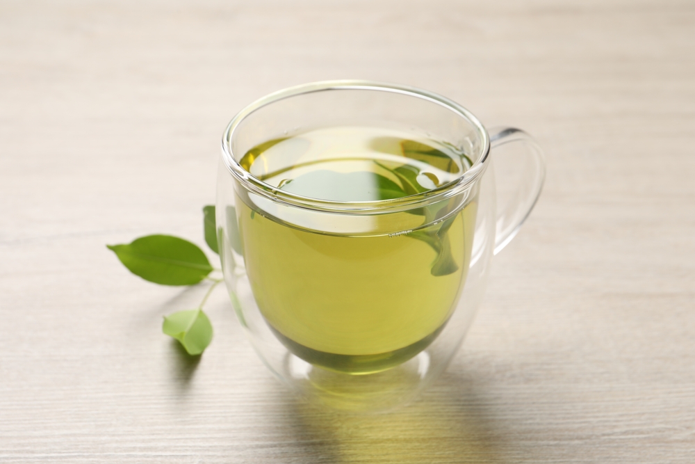 Refreshing green tea in cup and leaves on wooden table, closeup