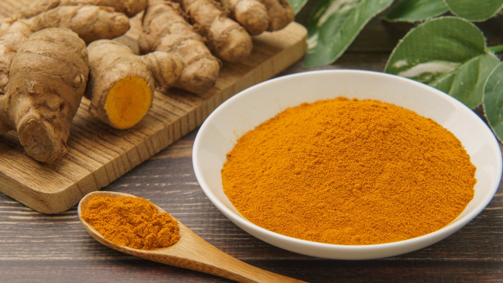 Turmeric and turmeric powder on wood grain background.