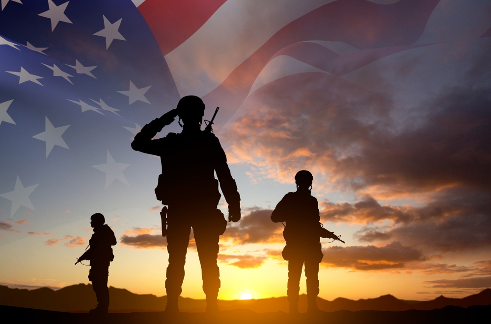 Silhouettes of a soldiers with USA flag against the sunset. Veterans Day. Honoring All Who Served
