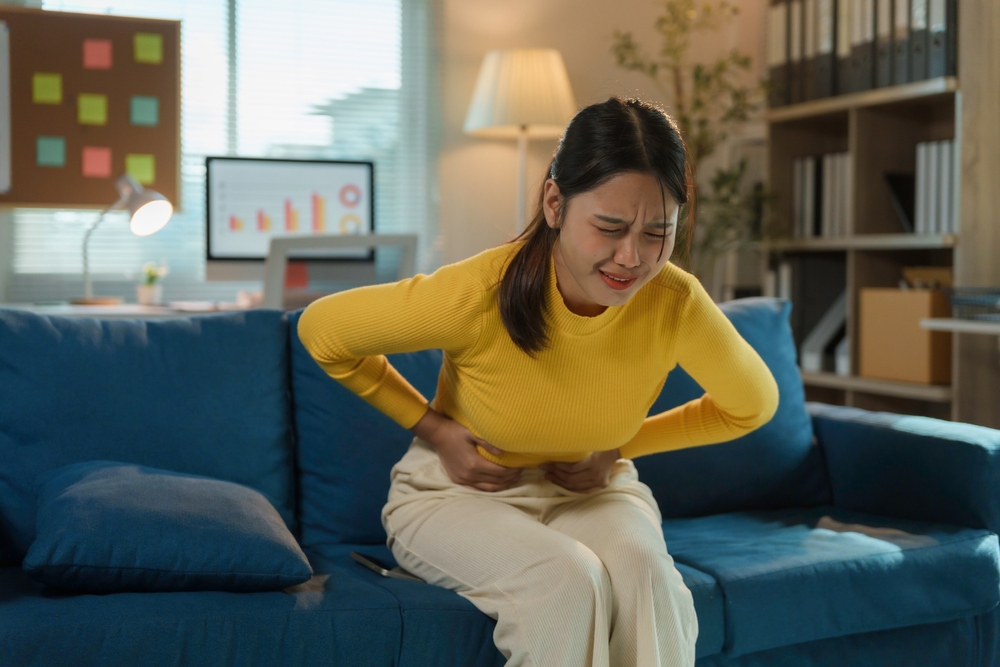 Young businesswoman is experiencing severe menstrual cramps while sitting on a sofa in her home office