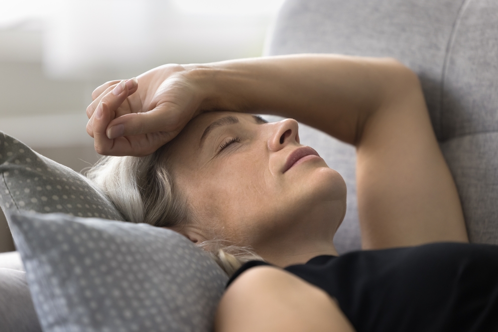 Weak senior woman lie on sofa keep arm on head feel pain dizzy headache suffer from menopause symptoms low blood pressure. Fatigue aged female relax on soft pillow sleep at daytime too tired from heat