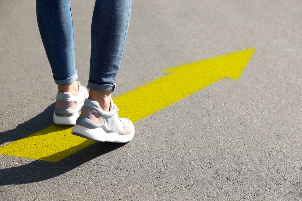 Woman walking on asphalt road with yellow arrow, closeup. Move forward