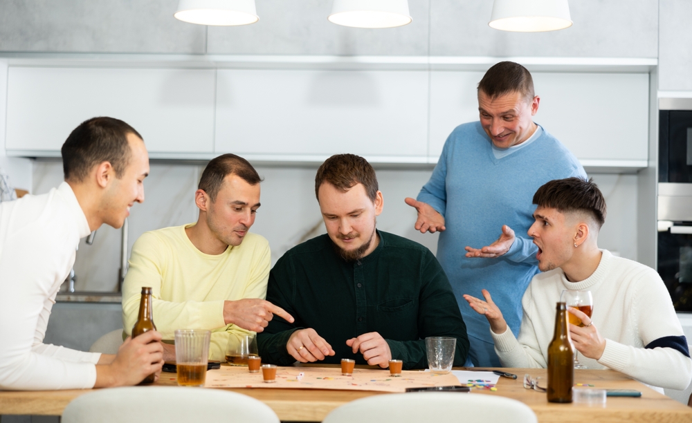 Lively group of men spending free time together during bachelor gatherings, engaged in drinking board game, where losing turn meaning taking shot, in warm friendly home environment..