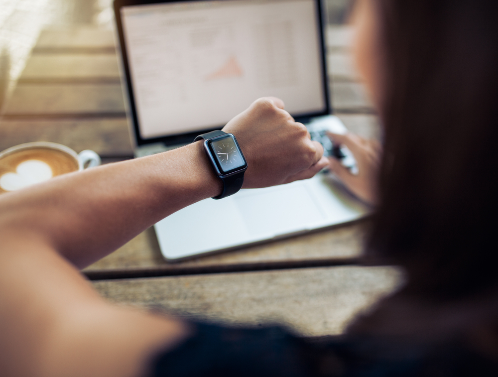 Close up shot of a woman checking time on her smartwatch. Female sitting in cafe with a laptop and cup of coffee.