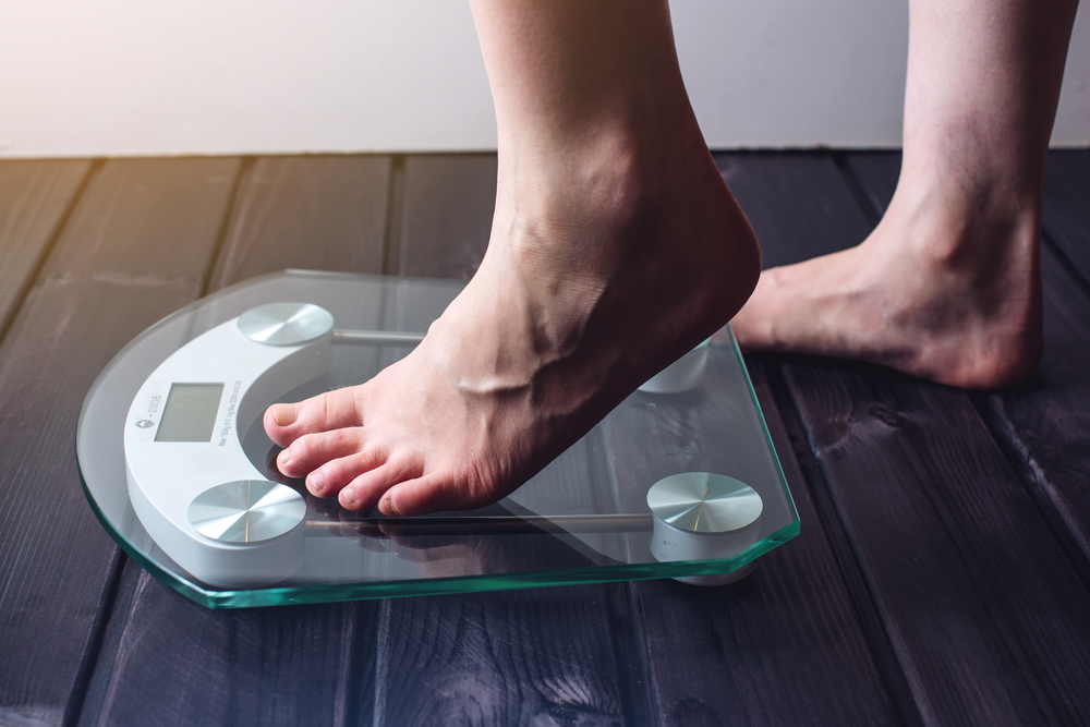 Female feet standing on electronic scales for weight control on wooden background. The concept of slimming and weight loss