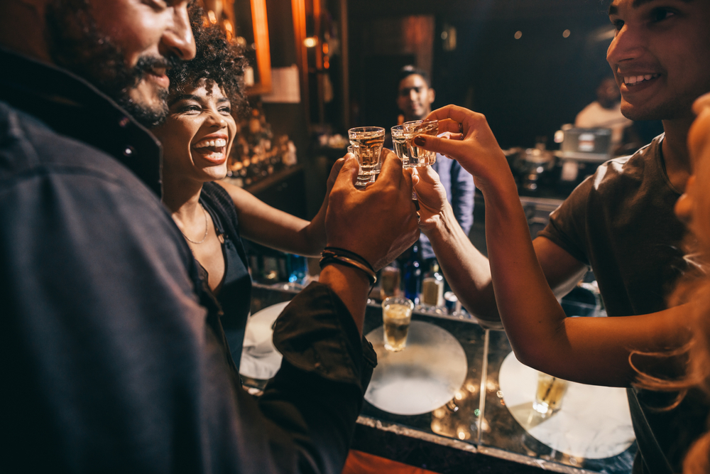 Friends toasting each other with shots of vodka as they enjoy a relaxing night out together at the pub. Group of friends together having fun