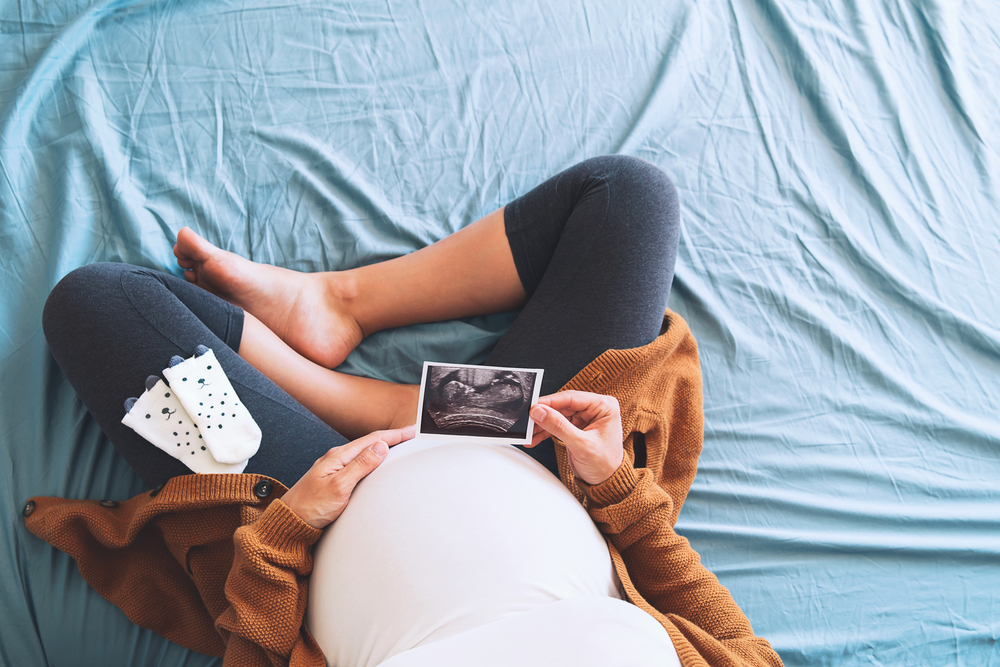 Pregnant woman holding ultrasound image. Concept of pregnancy, health care, gynecology, medicine. Young mother waiting of the baby. Close-up, copy space, indoors.