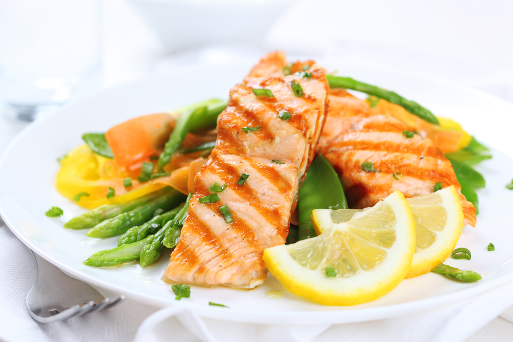 grilled salmon with asparagus, pea, yellow peppers, carrots and spring onions on white plate