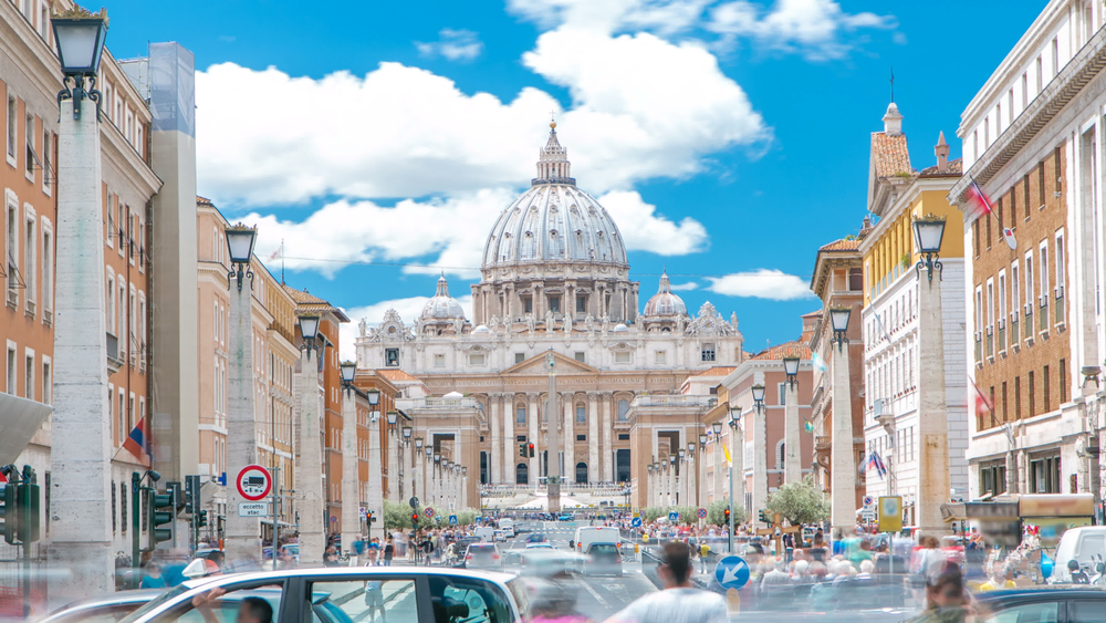 Rome, Italy, Vatican: St. Peter's Basilica in Vatican City State view from Via della Conciliazione, Road of the Conciliation. Blue cloudy sky with traffic on the road