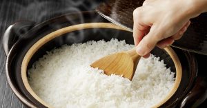person spooning out cooked rice from a rice cooker using a wooden spoon
