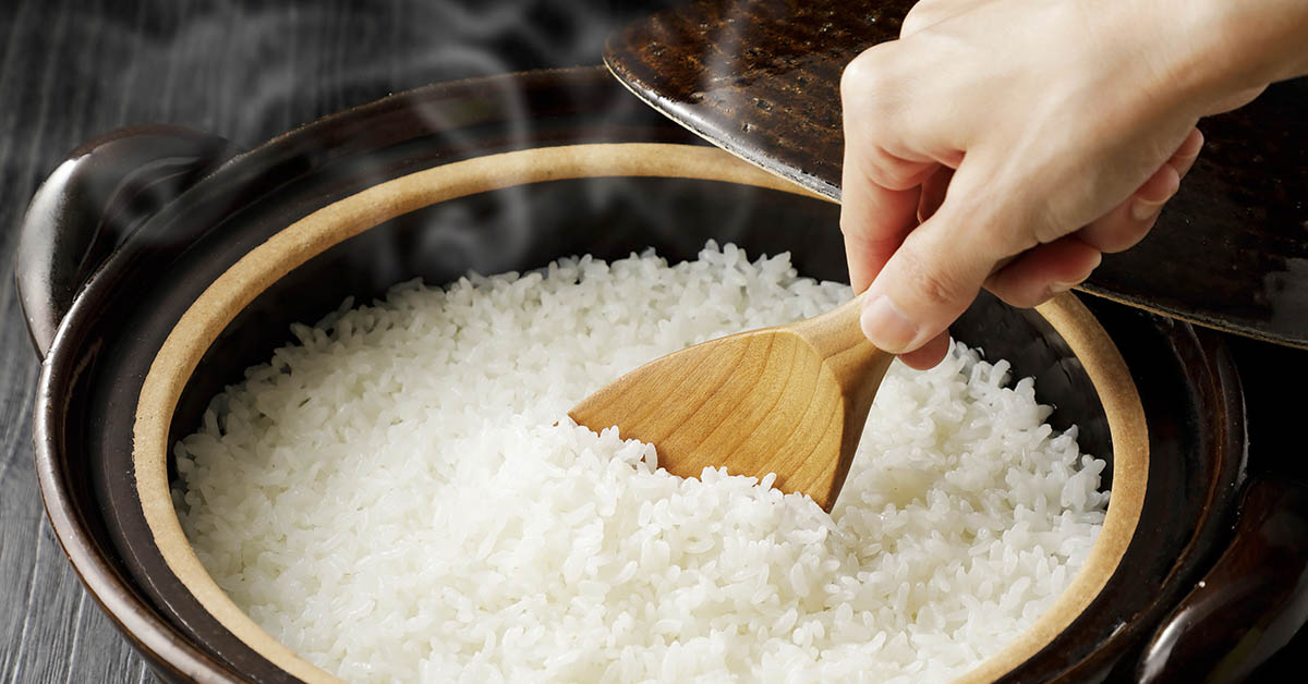 person spooning out cooked rice from a rice cooker using a wooden spoon