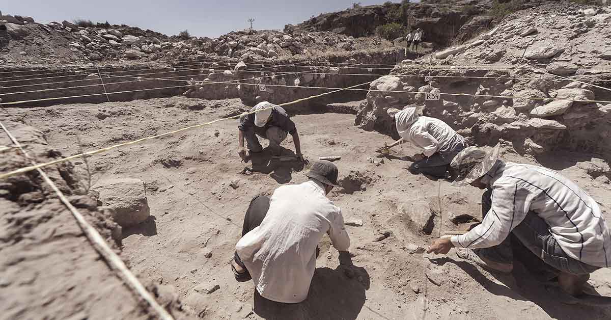 archaeologists working in a field, likely during an excavation, using specialized tools