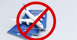 Model plane sitting on top of passports with red cross over top. Travel ban concept