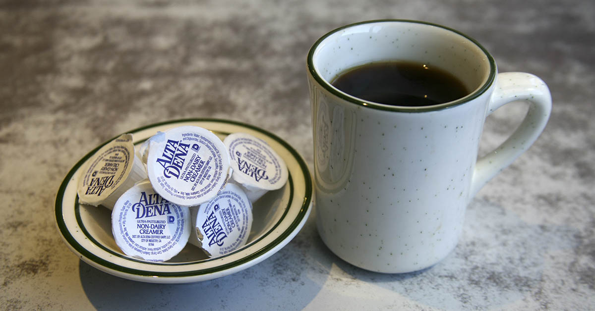 Cup of coffee beside a small bowl filled with individual non-dairy coffee creamers