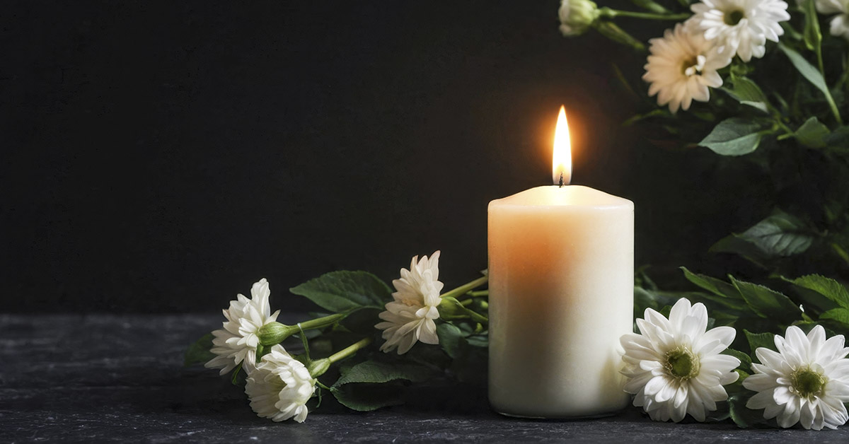 lit white candle with white flowers placed beside it. Vigil, funeral concept