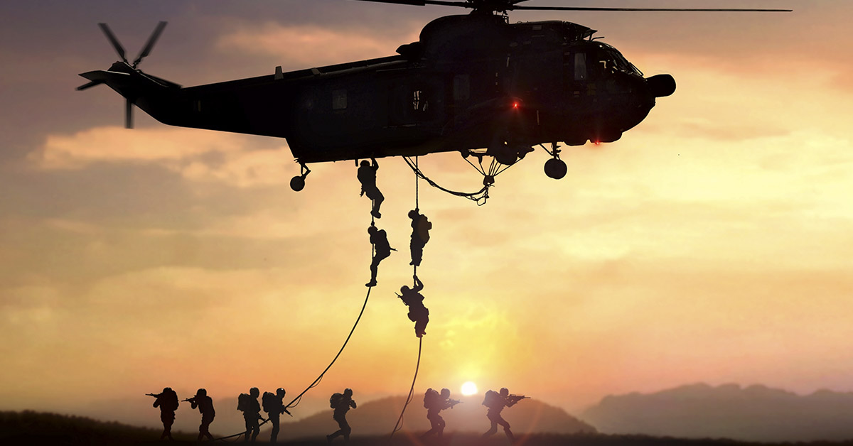 Military helicopter with soldiers rappelling down on ropes