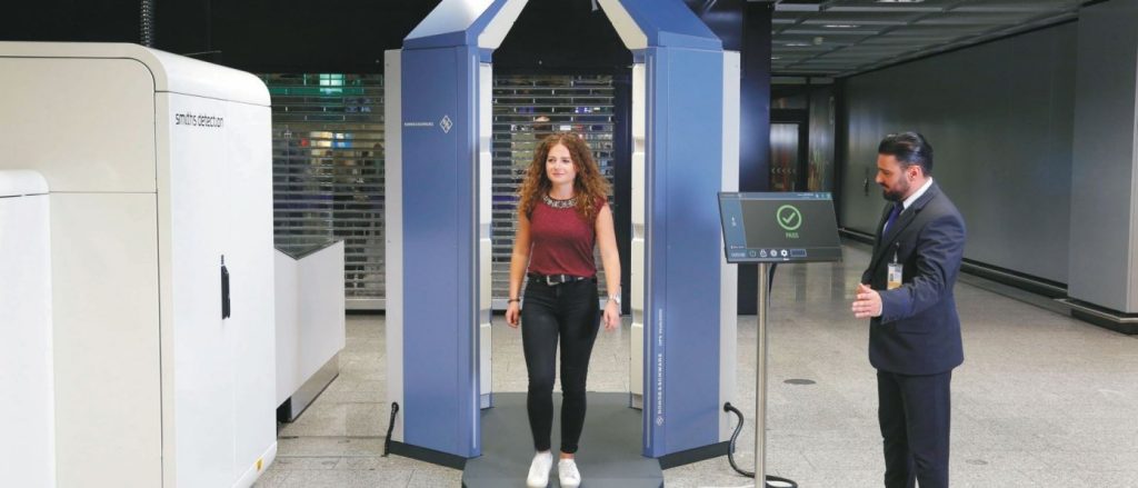 Passenger walking through advanced airport security scanner while officer monitors.