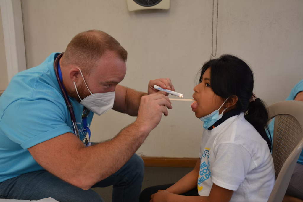 Medical professional in light blue scrubs administering a nasal swab test to a young patient wearing a mask, demonstrating the testing process recommended for those experiencing severe throat symptoms.