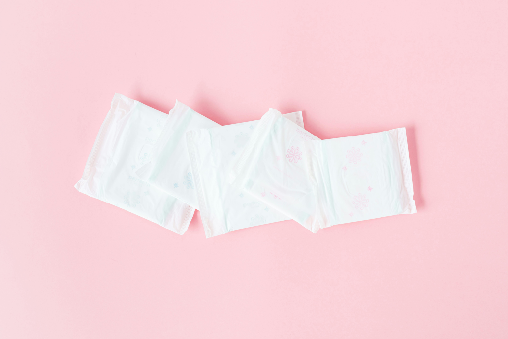 Five white menstrual pads arranged on a pink background.