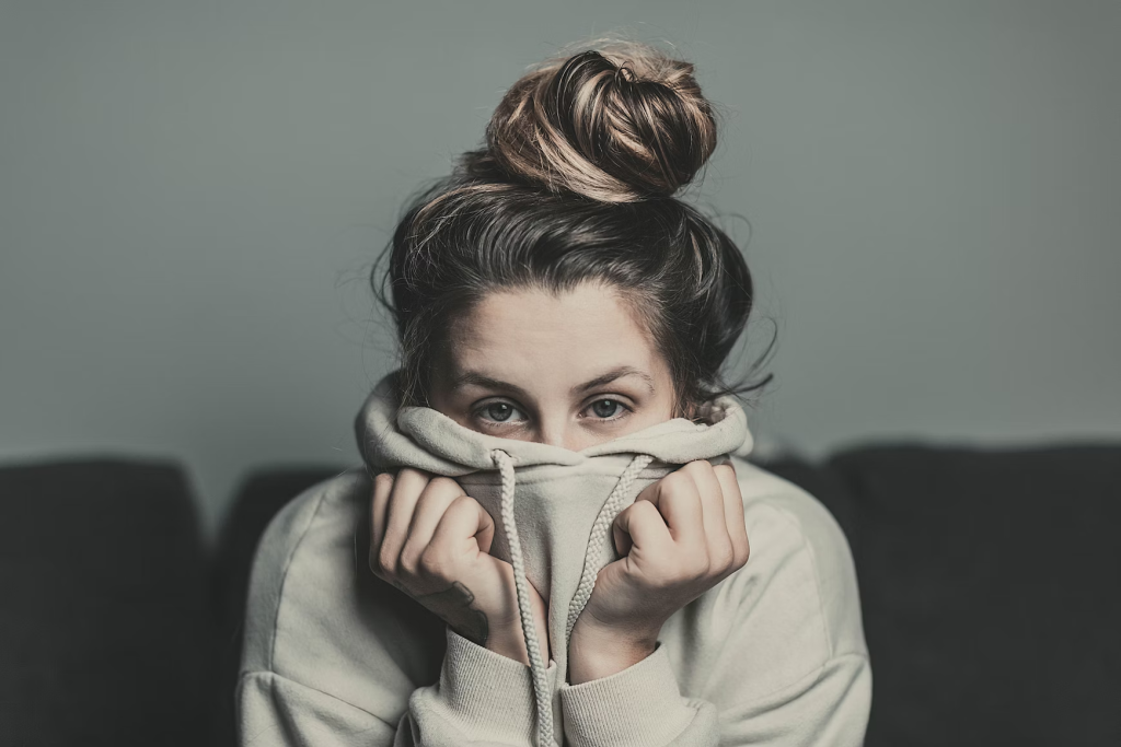 woman with her face half covered by her hoodie, showing signs of stress and anxiety, which is an uncommon cause of hives.