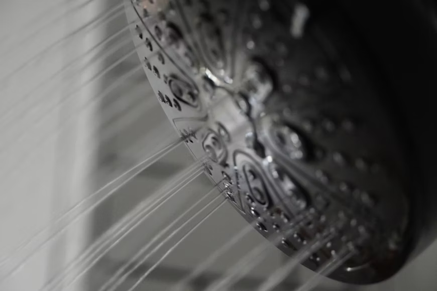 shower head with water flowing form it. Hot showers can be an uncommon cause of hives