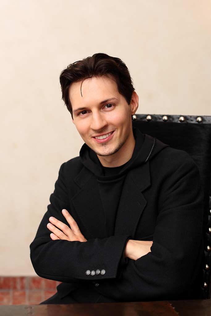 Pavel Durov in a dark suit with arms crossed, smiling confidently.