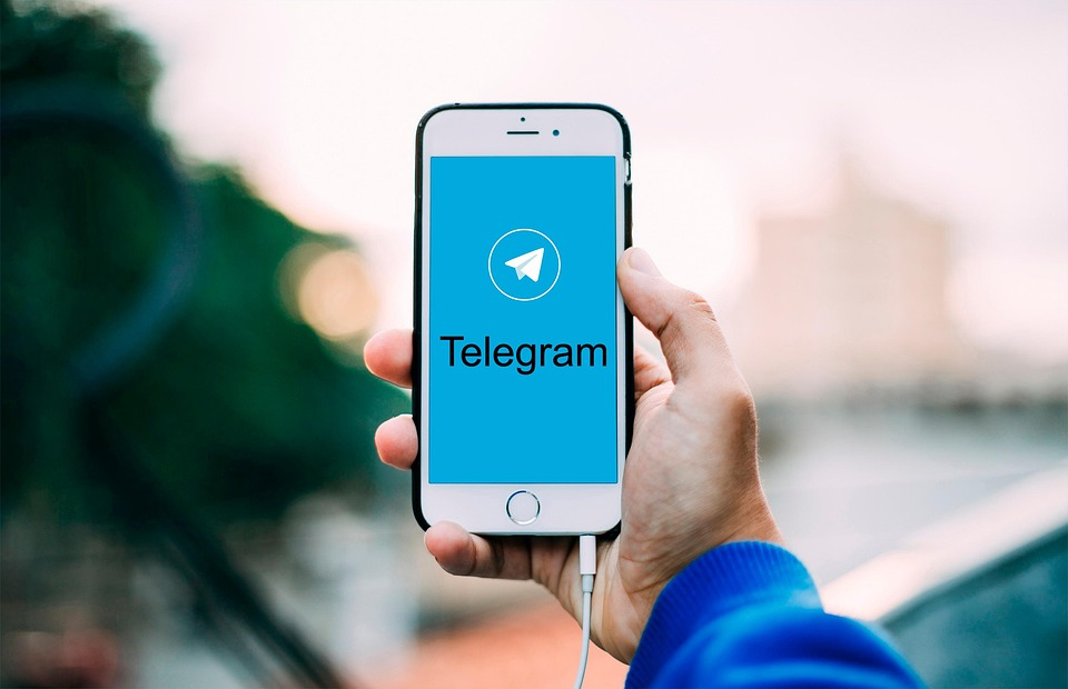 Hand holding smartphone displaying Telegram app logo on blue background.
