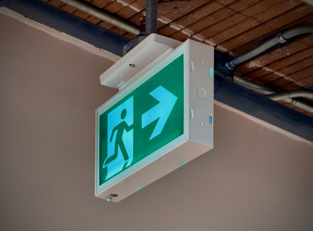 Green exit sign with running figure and directional arrow for emergency evacuation.